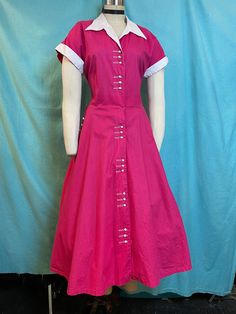 "1950s W:32 Dark Pink Magenta cotton fit and flare white pique collared short sleeve button up dress with pockets! Vintage 50s beautiful fit and flare dress. Made out of solid dark pink/magenta cotton with cotton pique white contrast. Bodice darted, with cuffed sleeves and collared neckline. Rows of 3 plastic buttons that looks like a small toothpaste caps. One of a kind. Unlined. Added petticoat not included.  MEASUREMENTS  Bust: 40\" Waist: 32\" Hips: free Bodice length: 18\" Skirt length: 30\" with no hem available to let down This is in good vintage condition, overall wear to fabrics due age, presents beautifully and is completely wearable as is! ✨" Classic Short Sleeve Shirt Dress With Buttons, Fitted Vintage Dress With Short Sleeves, Fitted Cotton Dress With Collared Neckline, Retro Short Sleeve Dress With Buttons, 1950s Style Vintage Short Sleeve Dress For Work, Classic Short Sleeve Dresses With Covered Buttons, Fitted Cotton Short Sleeve Shirt Dress, Classic Short Sleeve Dress With Button Cuffs, Fitted Cotton Shirt Dress With Placket