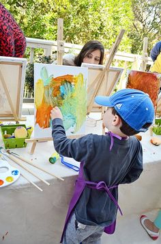 a young boy painting on an easel with other children around him at a table