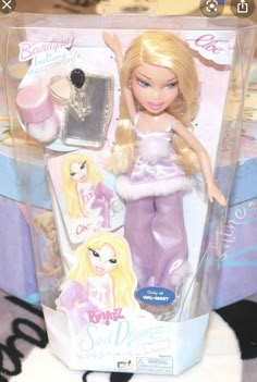 a barbie doll with blonde hair and purple pants in a box on top of a bed