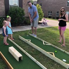 three adults and two children playing mini golf on the lawn in front of a house