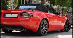 a red sports car parked in front of a gated area with two cars behind it