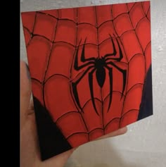 a hand holding up a piece of paper with a spider - man painting on it