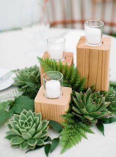 the table is set with candles and succulents on top of wooden blocks