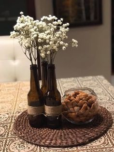 three bottles with flowers in them are sitting on a table next to a bowl of nuts