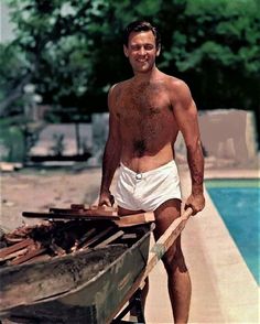 a shirtless man holding a wooden boat near a pool