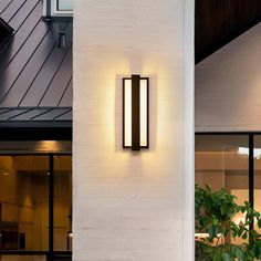 a modern outdoor wall light on the side of a white brick building with black trim