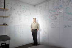 a man standing in front of a whiteboard with lots of writing on the wall