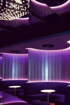 a purple room with round tables and lights on the ceiling, along with two couches that are facing each other