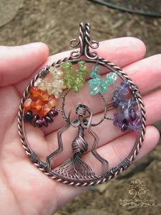 a hand holding a tree of life pendant with seven chakras in the center