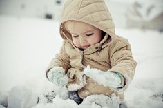 a little boy playing in the snow with his mittens and gloves on, wearing a tan jacket