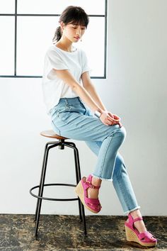 a young woman sitting on top of a stool next to a window wearing pink shoes