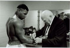 a man in a suit and tie standing next to another man with no shirt on