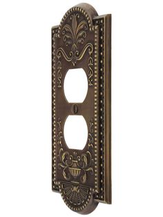 an ornately decorated switch plate covers the face of a single outlet in antique brass