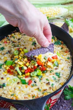 a person dipping a tortilla chip into a skillet filled with corn and vegetables