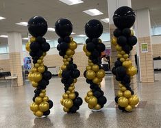 three tall black and gold balloons are in the middle of an empty floored room