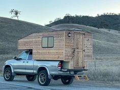 a truck with a wooden cabin on the back is parked in front of a grassy hill