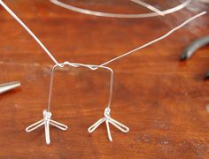 a pair of silver earrings sitting on top of a wooden table next to scissors and wire