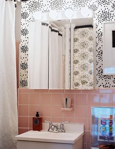 a bathroom with pink tile and white fixtures, including a mirror over the sink that has black flowers on it