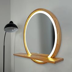 a round mirror sitting on top of a wooden shelf in front of a wall mounted lamp