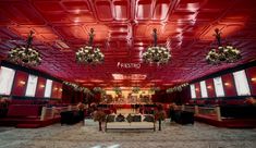 the interior of a restaurant with red walls and ceiling tiles, decorated with floral arrangements