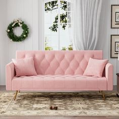 a pink couch sitting in front of a window next to a rug and table with a wreath on it