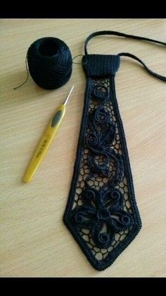 a crocheted neck tie next to a ball of yarn and a knitting needle