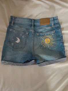 a pair of denim shorts with embroidered sun and moon patches on them sitting on a bed