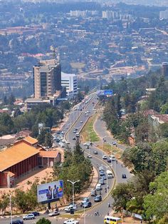 a city street filled with lots of traffic next to tall buildings and green trees in the background