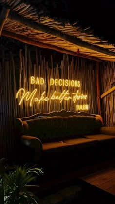 a couch sitting under a neon sign in front of a bamboo wall with writing on it