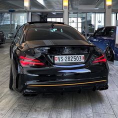 the back end of a black car parked in a showroom with other cars behind it