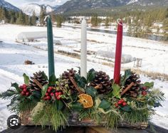 a wooden table topped with two candles and christmas decorations on top of snow covered ground