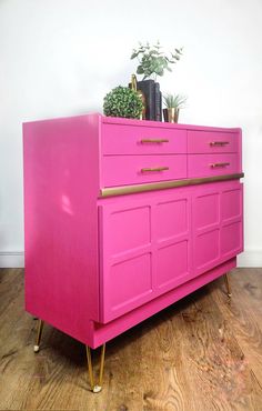 a pink dresser sitting on top of a wooden floor next to a potted plant