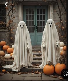 two ghost statues in front of a house with pumpkins