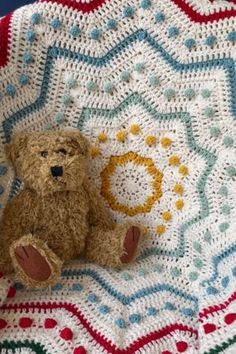 a brown teddy bear sitting on top of a crocheted blanket in the shape of a circle