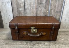 an old brown leather suitcase sitting on top of a wooden floor next to a wall