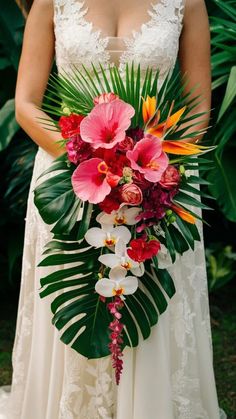 a woman in a wedding dress holding a large bouquet of flowers and greenery on her arm