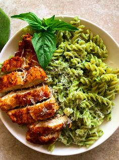 a white plate topped with pasta and meat covered in pesto next to an avocado