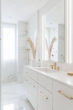 a white bathroom with gold accents and marble counter tops, along with large mirrors on the wall