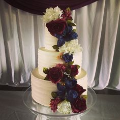 a three tiered cake with flowers on the top and bottom is sitting on a clear plate