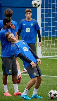 two soccer players in blue shirts are playing with a ball on the field while another player looks on