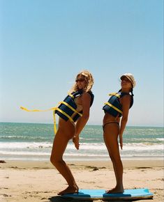 two women in bathing suits standing on a surfboard