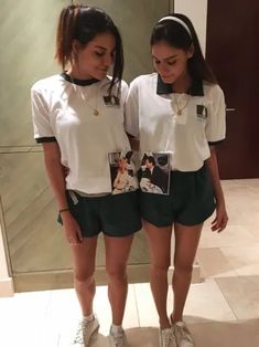 two young women standing next to each other in front of a mirror wearing matching outfits