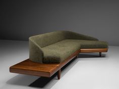 a green couch sitting on top of a wooden table next to a gray wall and floor