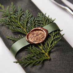 a wax stamp is placed on top of a black napkin with green ribbon and pine needles