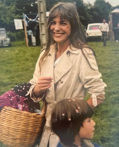 an old photo of a woman holding a basket with two children in the grass behind her