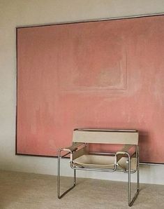 an empty chair sitting in front of a pink wall with a painting on it's side