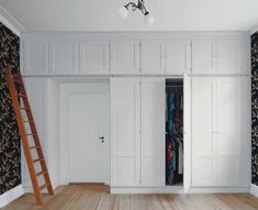 an empty room with white closets and black wallpaper on the walls next to a ladder