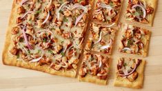 several square pieces of pizza with onions and meat toppings on them sitting on a wooden surface