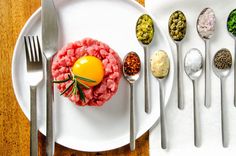 a white plate topped with meat and vegetables next to spoons