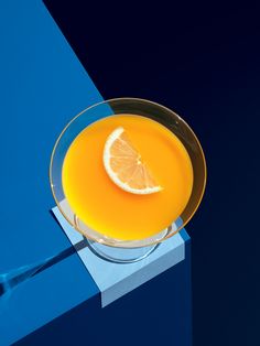 an orange juice in a glass with a slice of lemon on the rim and blue background